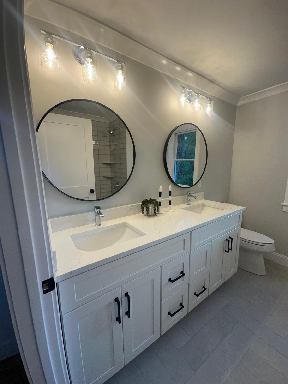 Finished bathroom remodel with a white double vanity, black round mirrors, glass sconces and large-format grey floor tile