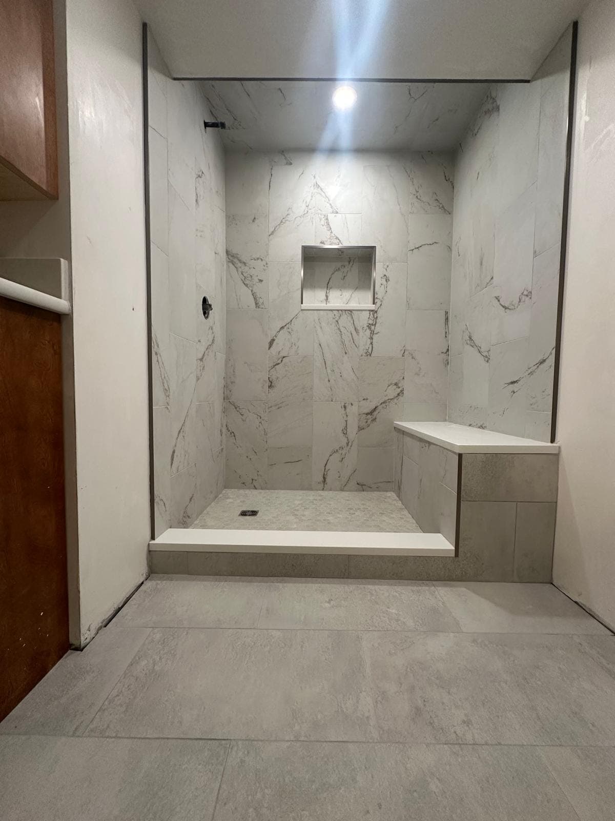 Curbless marble shower with a built-in bench and recessed niche, built over a waterproofed and sloped pan