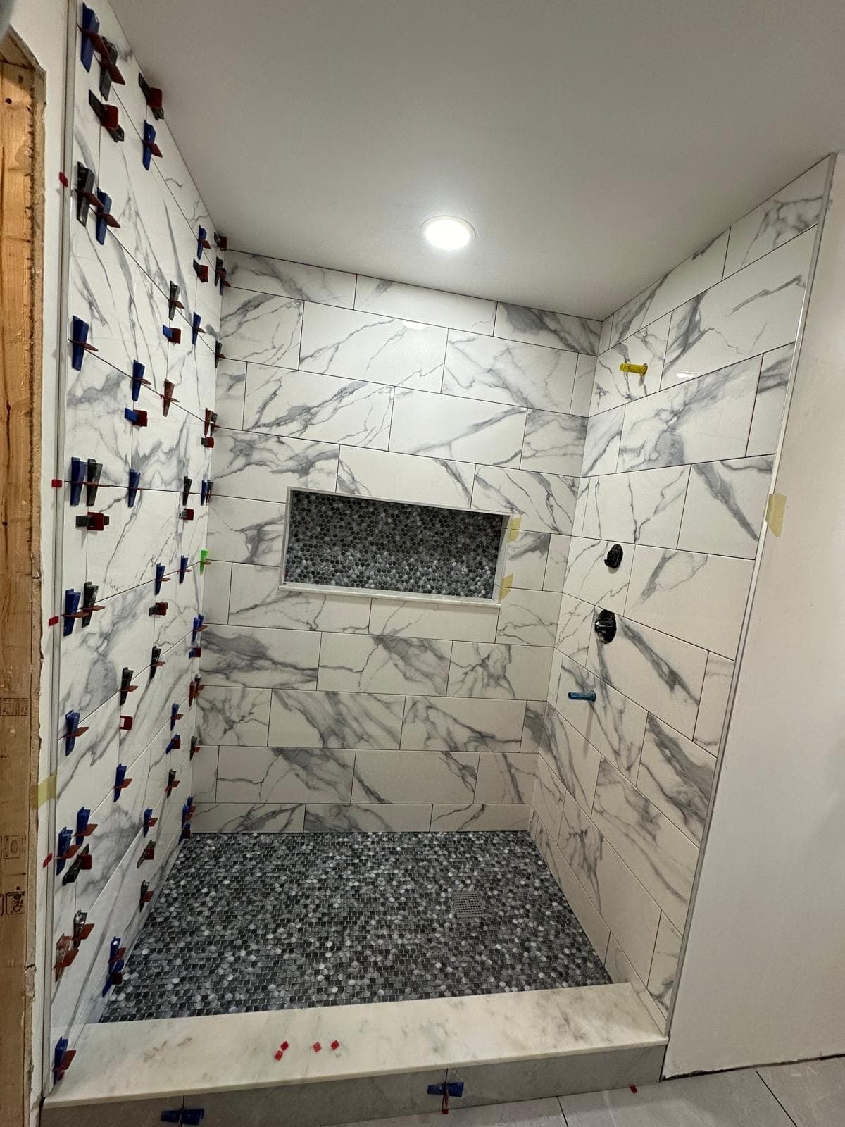 Marble shower walls mid-installation with levelling clips still in place holding the tiles on one plane